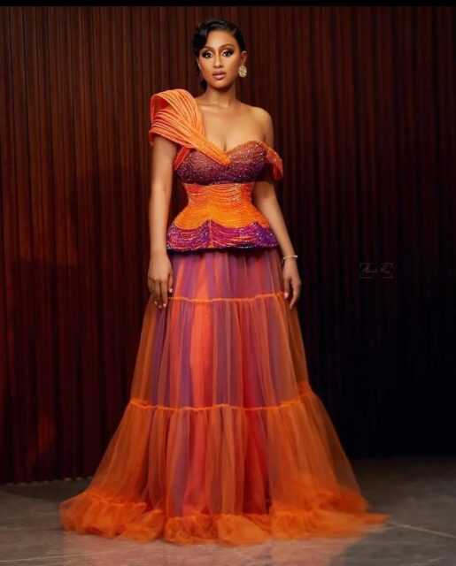 Woman in colorful off-shoulder gown standing.