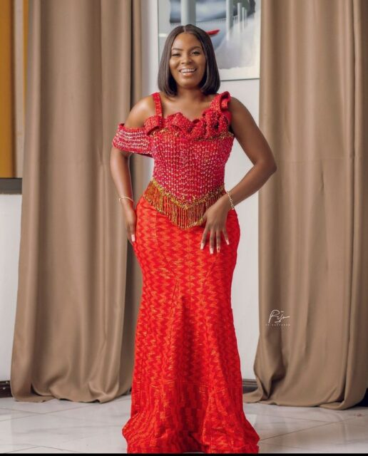 Woman in elegant red African print gown smiling.