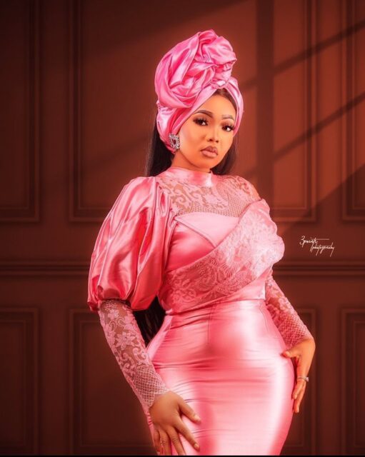 Woman in elegant pink dress and headwrap posing.